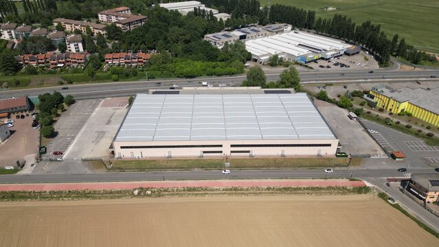 Aerial View of a Large Industrial Warehouse: An expansive industrial complex with a vast warehouse structure featuring a modern, grid-like roof is seen from above.