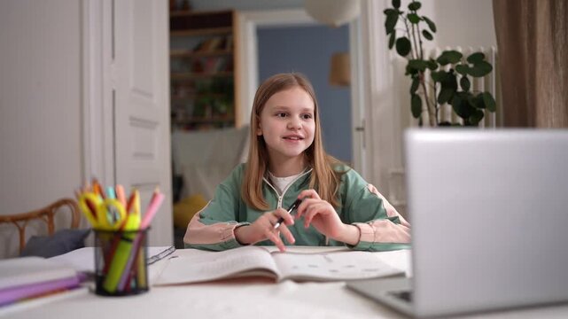 Caucasian girl smiling at laptop screen, engaged in online class with textbook open and colored pens in foreground, braided hair, cozy study corner, daylight .
