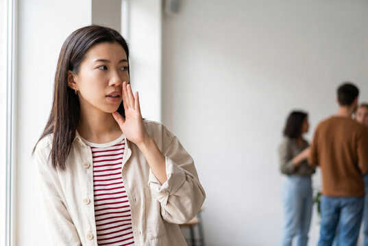 Woman whispering with hand near mouth, sharing secret or gossip about defocused people