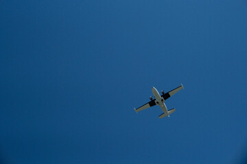 Fototapeta premium Low Angle View of a Twin-Engine Propeller Plane Flying in Clear Blue Sky on Sunny Day