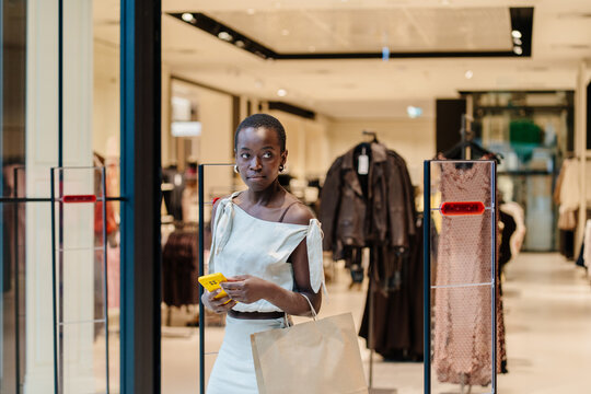 Stylish Black Woman with Shopping Bag Using Phone in Apparel Showroom