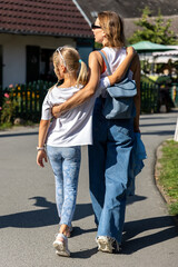 Obraz premium Mother daughter walk suburban street arms embrace bond warmth everyday life. Sunny outdoor scene reflects care, trust, and close family connection calm residential neighborhood vacation trip