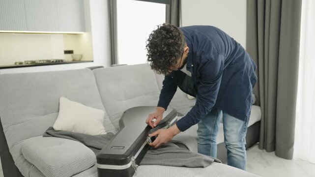 Man packing an acoustic guitar into a case while standing next to a sofa at home