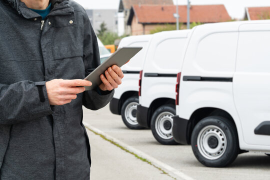 Fleet manager with digital tablet supervising rows of white delivery vans