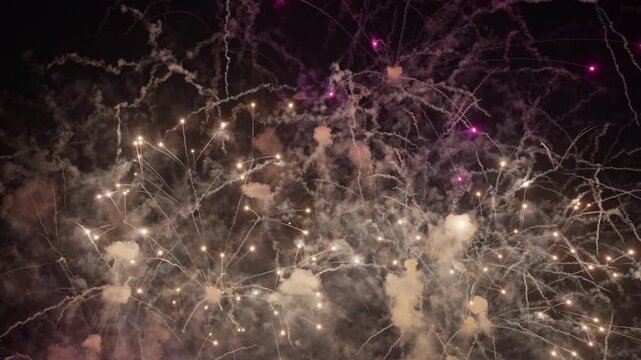 Stunning fireworks explosion fills the dark night sky over Dubai with brilliant golden sparks and vibrant purple hues. Smoke trails create dramatic patterns as pyrotechnics burst in celebration.