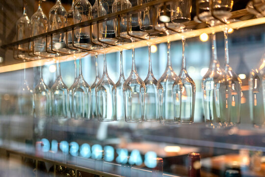 Elegant wine glasses hanging upside down on a bar rack, illuminated by warm golden lights in a restaurant setting.