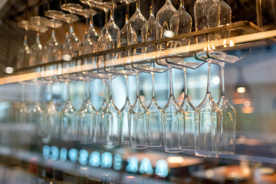Rows of clean wine glasses hanging upside down on a rack above a bar, reflecting blue ambient light in an elegant restaurant.