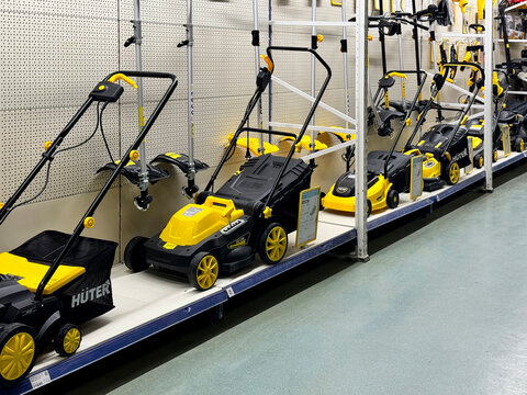 Barnaul, Russia, 06.06.2025: Huter brand electric lawn mowers and garden tools displayed on retail store shelves, yellow and black color scheme. Garden equipment for sale.