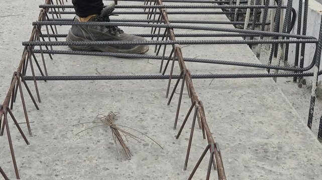 Side view of a steel fixer placing a stirrup bar on the floor slab and securing it with binding wire.