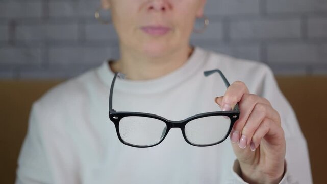 Woman cleaning eyeglasses with spray and cloth. Careful woman spraying a cleaning solution on her eyeglasses and wiping the lenses with a blue microfiber cloth for better vision