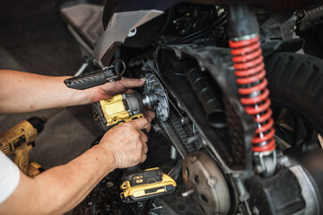 Obraz premium Mechanic using electric impact wrench to repair motorcycle CVT transmission system.