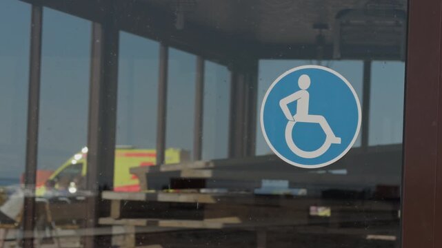 Wheelchair accessible sign on glass door reflecting runway vehicles and terminal interior, blue disability icon for navigation, modern inclusive travel atmosphere, crisp k clarity