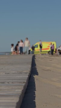 Paramedics swiftly assist near dunes. Ambulance team prepares for urgent medical transfer. Vigilant emergency responders enact quick rescue amidst sandy dunes with dramatic lighting