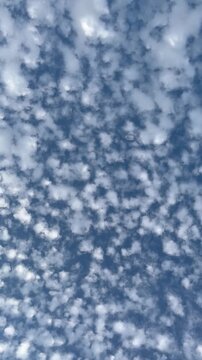 Vertical shot of white fluffy clouds on a bright blue sky background