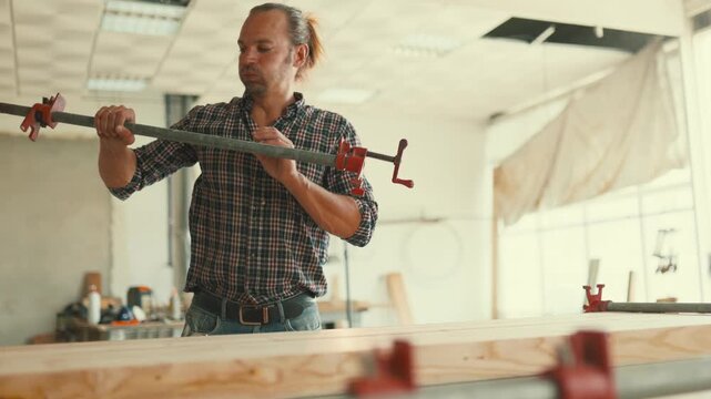 Carpenter using clamps on a wooden plank in a workshop