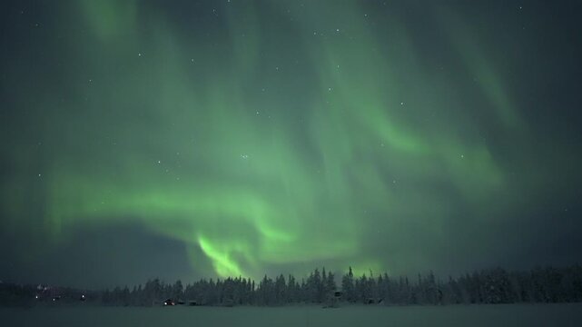 Aurora borealis over snowy forest landscape with cabins, real time