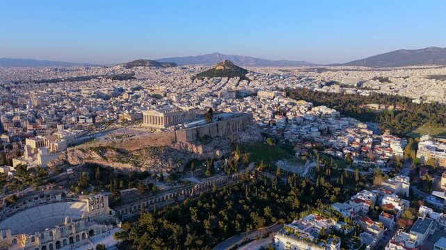 Aerial video of the Acropolis of Athens, the Parthenon, and the Odeon of Herodes Atticus, with the city landscape and mountains during the golden hour.