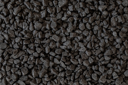 Black gravel stone background. A top view of a dense, evenly spread layer of small, irregular decorative stones. Dark charcoal color, rough and particulate texture.