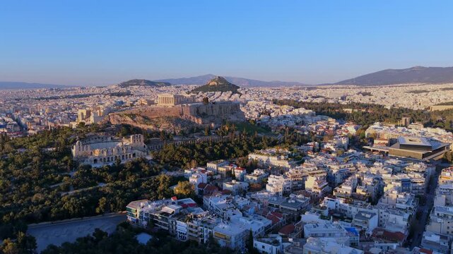 Aerial video of the Acropolis of Athens, the Parthenon, and the Odeon of Herodes Atticus, with the city landscape and mountains during the golden hour.