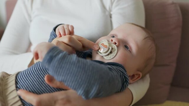 Portrait of a young mother gently holding her adorable baby son who is using a pacifier to stay calm. This authentic moment captures the essence of motherhood, care, and peaceful bonding in a cozy