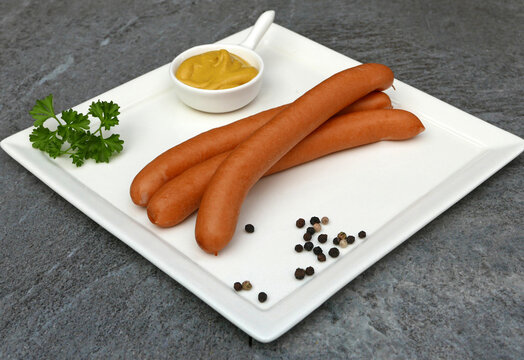 Vienna sausages with mustard and parsley on a white, stone-effect plate.