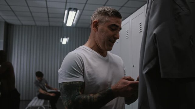 Three Athletic Male Airport Security Officers in Uniform in Locker Room. One Officer Checking Smartphone and Interacting With Colleagues While Change After Their Shift. Professional Environment.