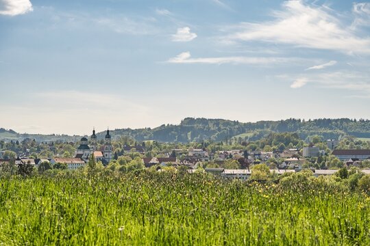 Panoramic view over Kempten with the St Lorenz Basilica and historic residence surrounded by green spring meadows and forests under a blue sky