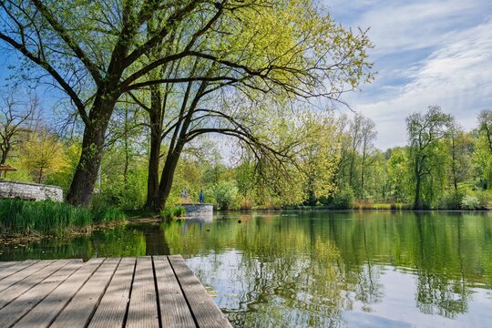 Spring landscape at Engelhaldepark in Kempten with a wooden jetty and green trees reflecting in the calm lake water
