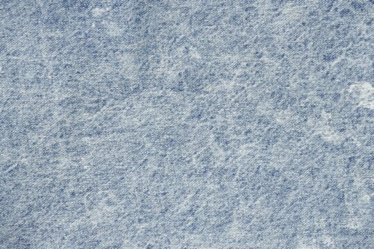 Full frame macro shot of light blue acid-wash denim material. Detailed textile texture background for fashion, apparel, and clothing design projects.