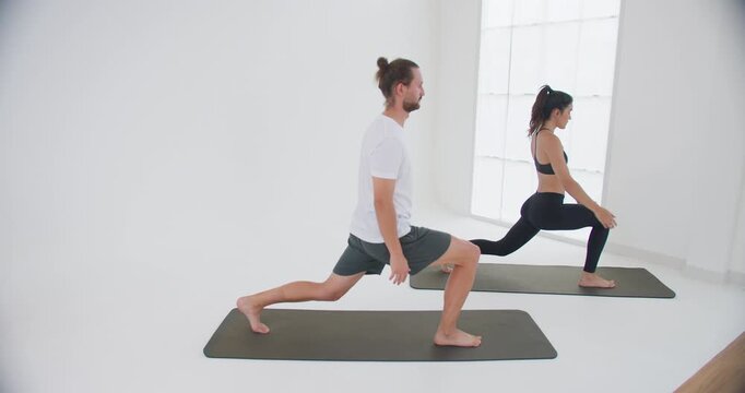 A focused couple practicing a warrior pose together, improving balance and flexibility during a yoga class in a bright, minimalist wellness studio.