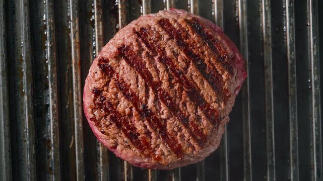 fresh ground beef burger meat patty cooking on hot grill, top view.  A beef patty with grill marks is fried on a hot grill, top view.