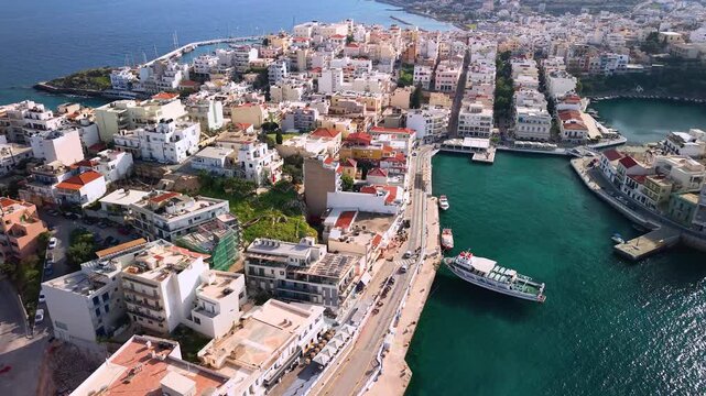 Agios Nikolaos Crete Greece 4k aerial drone view of Lake Voulismeni and colorful houses. Scenic circular lake in city center with boats and mountains in background. Unique Mediterranean travel scenery