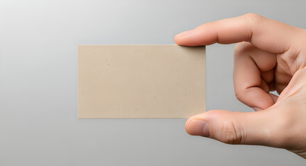 Obraz premium A hand holding a blank beige business card on a gray background