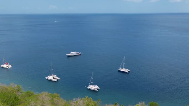 Aerial view of iconic Piton volcanic mountain rising above turquoise Caribbean waters in Saint Lucia. White sailboats and catamarans anchor in calm bay near tropical beach with lush green vegetation.