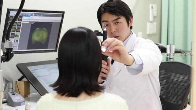 ペンライトで目の状態を診察する眼科医と女性患者の診療シーン(モニターはテスト画面のはめ込み)