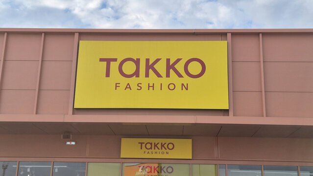 A yellow storefront sign for Takko Fashion on a pinkish-tan building facade under a cloudy sky. Picture taken on May 2, 2026 in Ploiesti, Romania.