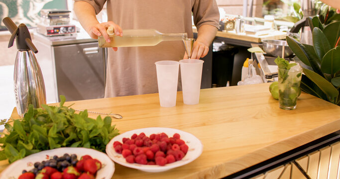 Alcohol pouring. Drink making. Unrecognizable barman hands preparing classic beverage using measuring tool into glass with crushed ice lime at workplace.