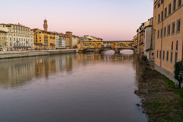 Fototapeta premium The iconic Ponte Vecchio bridge spans the Arno River in Florence, Italy, reflecting the warm hues of the twilight sky