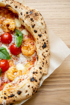 Italian pizza. Homemade dish. Fresh food with tomatoes melted cheese mozzarella shrimp green basil leaves with sauce on wooden table.