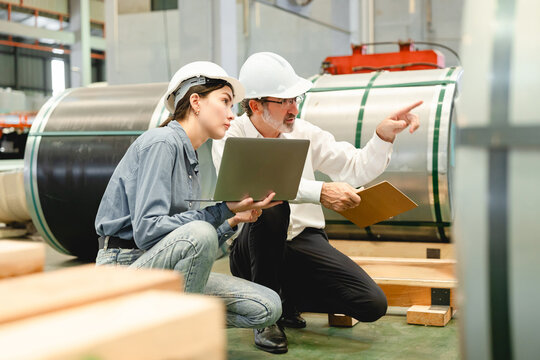 Caucasian man conducts detailed inspection of gray industrial machinery and equipment within factory setting while wearing white shirt and dark pants, emphasizing safety process and equipment maintena