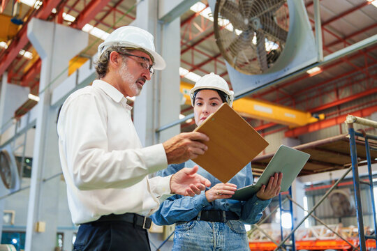 Two Caucasian men are meticulously examining metal sheets and cardboard box within warehouse environment, engaged in focused discussion with serious expression while inspecting production materials.