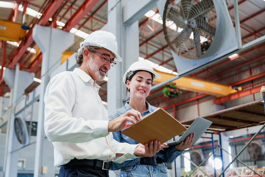 Two Caucasian men meticulously review architectural drawings within dimly lit metal sheet factory, focused on detailed inspection and process review for roof construction projects.