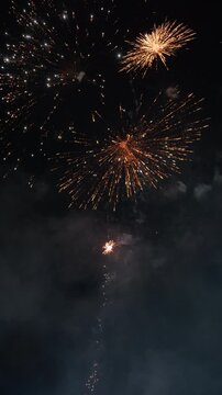 Large colorful firework exploding in dark night sky with vivid green and red trail radiating outward, golden spark scattered above, soft smoke cloud drifting below