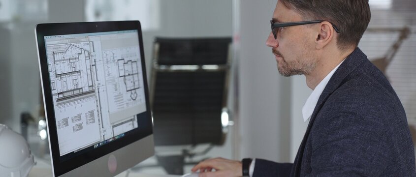 Architect working on building blueprint plans, creating design and engineering structure on desktop computer in office. Business and architecture concept