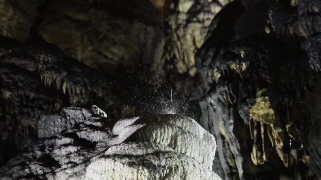 A view of dripping water on dripstone formations in a dark cave.