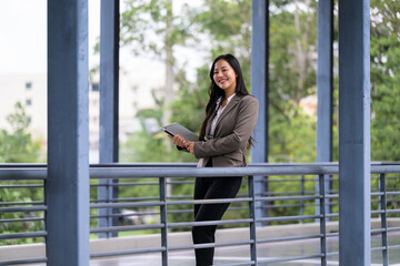 Fototapeta premium Asian businesswoman smiling holding digital tablet on modern bridge