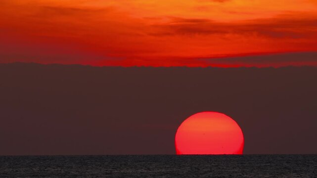 Cinematic sunset with a fiery red sun disappearing beyond the ocean horizon. Vibrant coastal landscape at twilight, ideal for vacation, wanderlust, and serene seascape concepts.