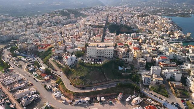 Agios Nikolaos Crete Greece 4k aerial drone view of luxury yacht marina and city panorama. Scenic reveal of coastal town architecture on hills in Mirabello Bay. Beautiful Mediterranean travel destinat