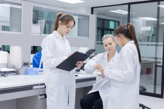 Three scientists in lab coats engage in discussion in laboratory