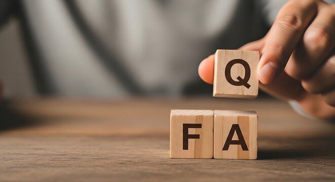 A person placing a wooden block with the letter Q on top of blocks spelling FA, representing frequently asked questions or FAQ, on a wooden table.